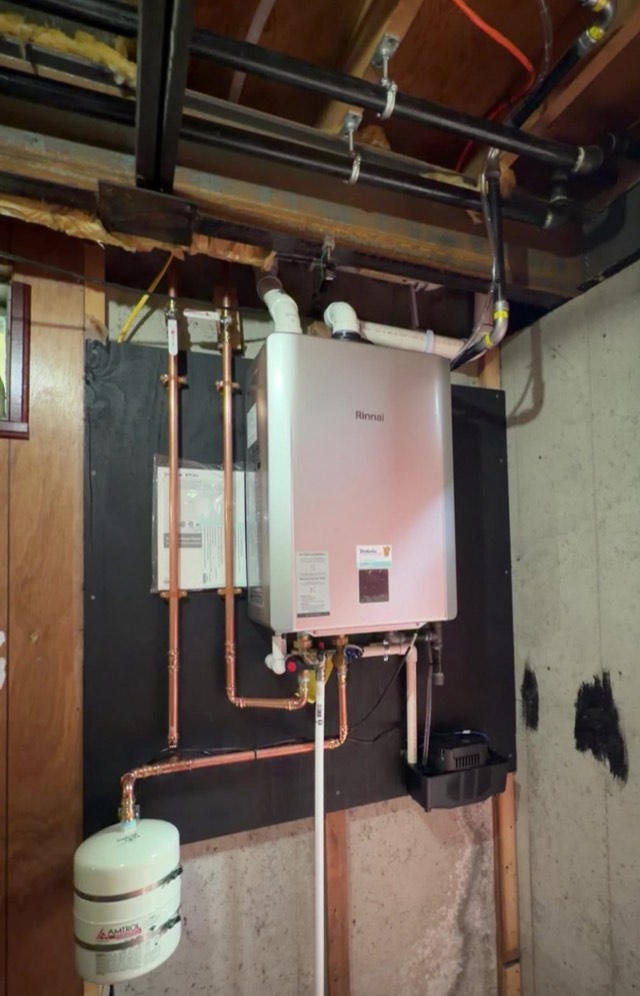 Tankless water heater installed in a basement with copper supply lines and an expansion tank