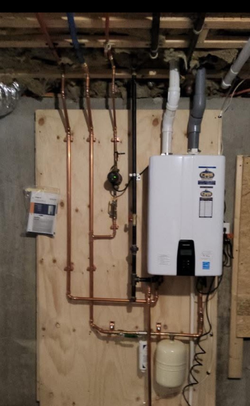 Navien tankless water heater mounted on a plywood board with new copper water lines, gas line, and vent piping